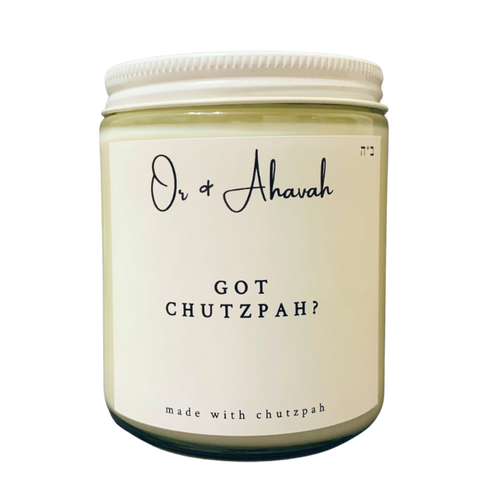 Clear glass candle with a white metal lid. Brand name is Or & Ahavah. Candle name is Got Chutzpah?. At the bottom, it says made with chutzpah. Scent notes are honey, coriander, bergamot, vanilla, oud wood, and tobacco leaf.