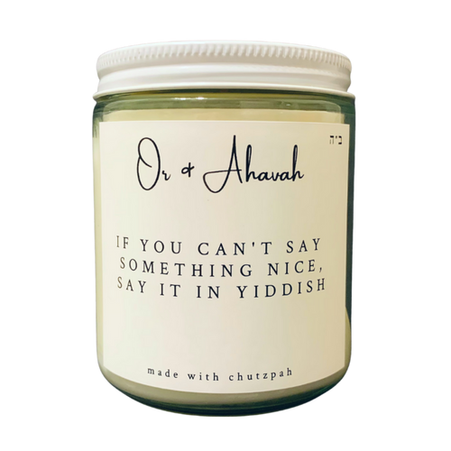 Clear glass candle with a white metal lid. Brand name is Or & Ahavah. Candle name is If You Can't Say Something Nice, Say It In Yiddish. At the bottom, it says made with chutzpah. Scent notes are fresh coffee, toasted hazelnut, maple, vanilla, and cream.