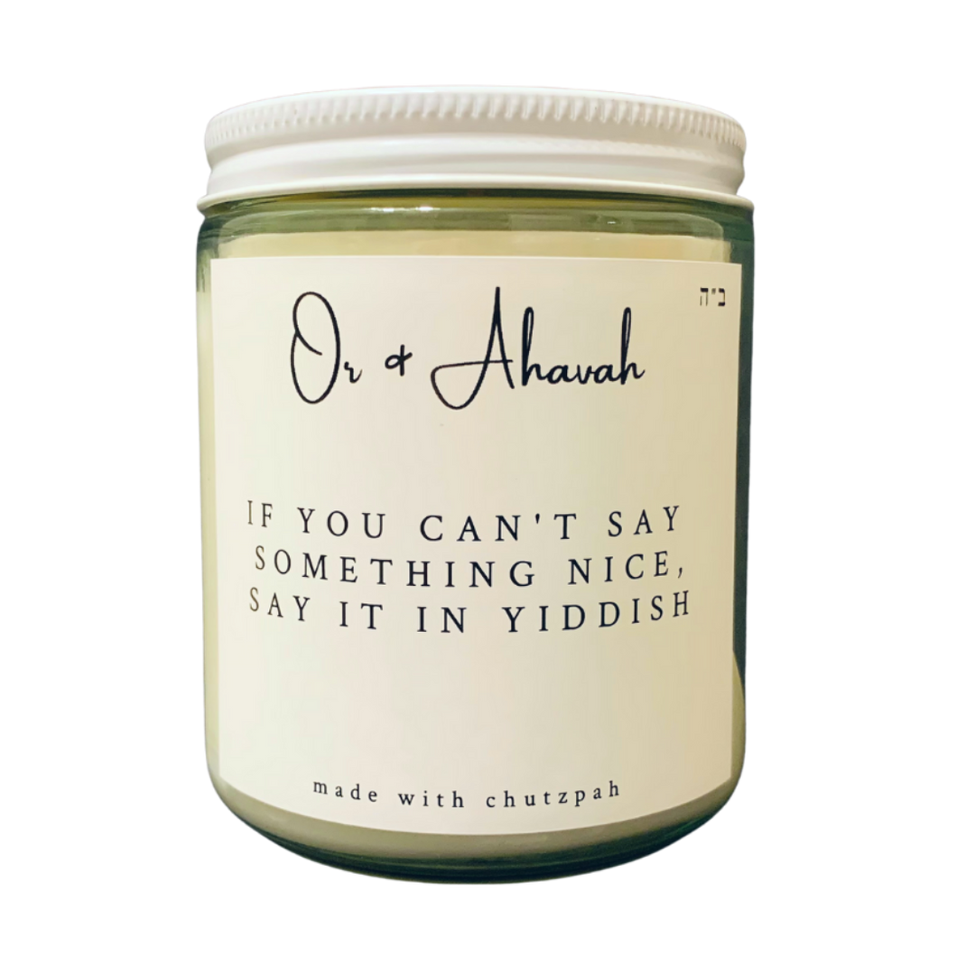 Clear glass candle with a white metal lid. Brand name is Or & Ahavah. Candle name is If You Can't Say Something Nice, Say It In Yiddish. At the bottom, it says made with chutzpah. Scent notes are fresh coffee, toasted hazelnut, maple, vanilla, and cream.